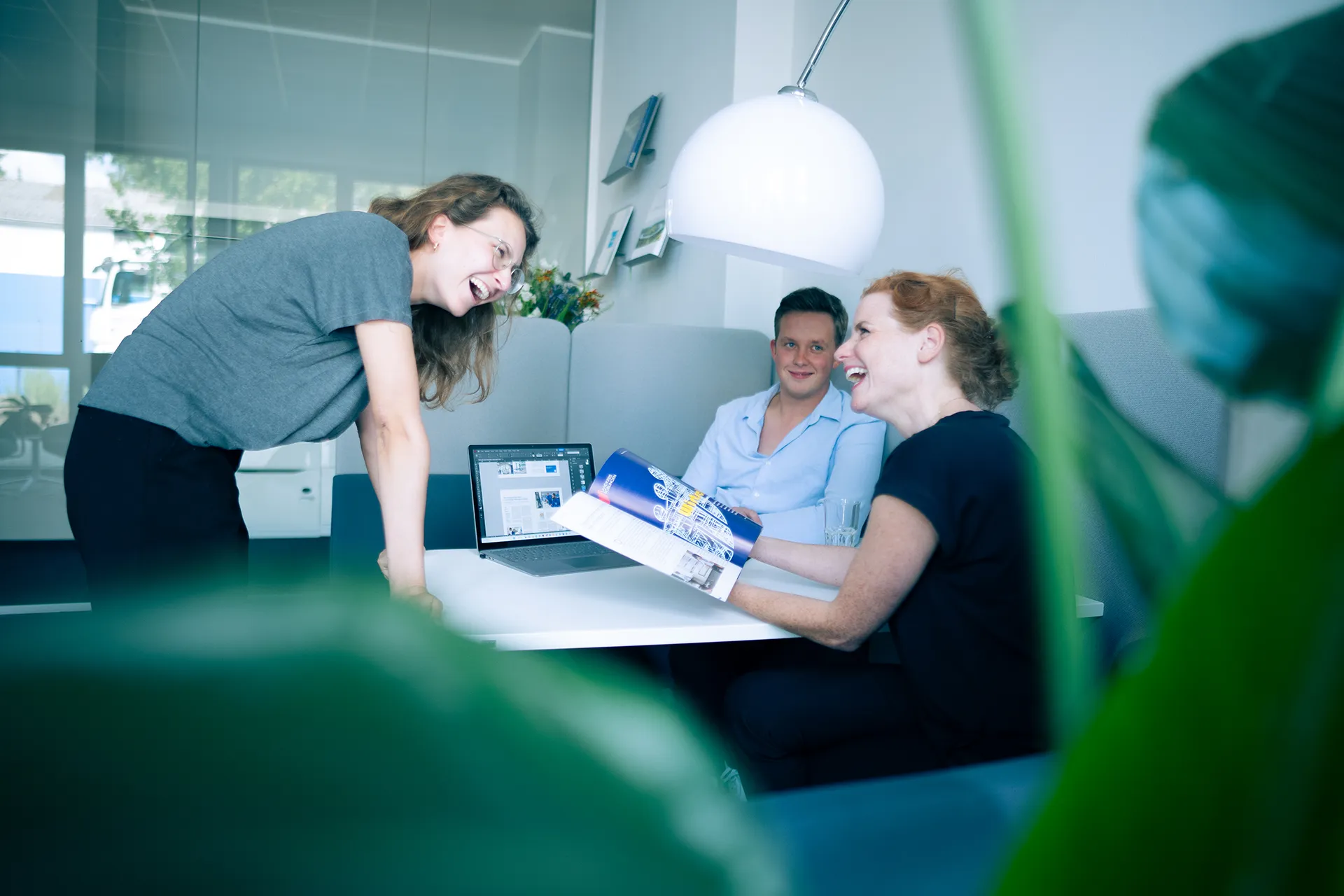 Drei Kolleg:innen lachen gemeinsam bei einer Besprechung